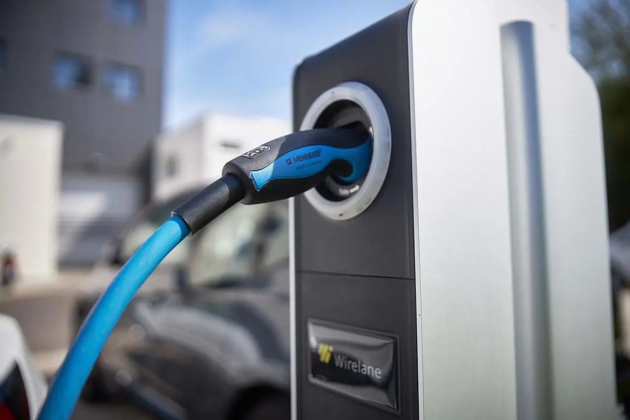 Ladesäule mit eingestecktem blauem Typ-2-Ladekabel, dahinter ein ladendes Elektrofahrzeug