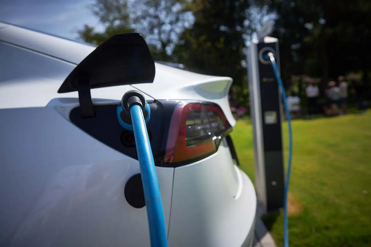 Weißes Elektrofahrzeug lädt über ein blaues Typ-2-Kabel an einer Ladesäule im Freien